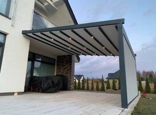 Pergola materiałową model Premium, kolor 7016ST, wersja przyścienna z oświetleniem LED, roletą boczną ZIP i tkaniną typu screen. Sterowanie na pilota firmy Somfy