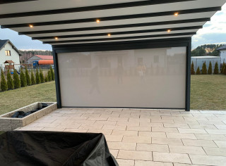 Pergola materiałową model Premium, kolor 7016ST, wersja przyścienna z oświetleniem LED, roletą boczną ZIP i tkaniną typu screen. Sterowanie na pilota firmy Somfy