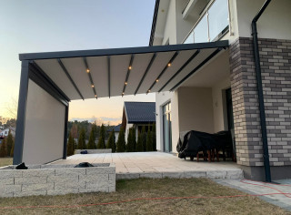 Pergola materiałową model Premium, kolor 7016ST, wersja przyścienna z oświetleniem LED, roletą boczną ZIP i tkaniną typu screen. Sterowanie na pilota firmy Somfy